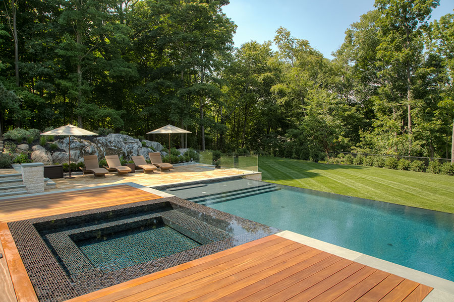 Elegant and minimalistic infinity pool featuring a wooden deck and jacuzzi, adorned with pool umbrellas and chairs, showcasing the exquisite pool renovation Elegant and minimalistic infinity pool featuring a wooden deck and jacuzzi, adorned with pool umbrellas and chairs, showcasing the exquisite pool renovation services in NY, NJ, and CT.