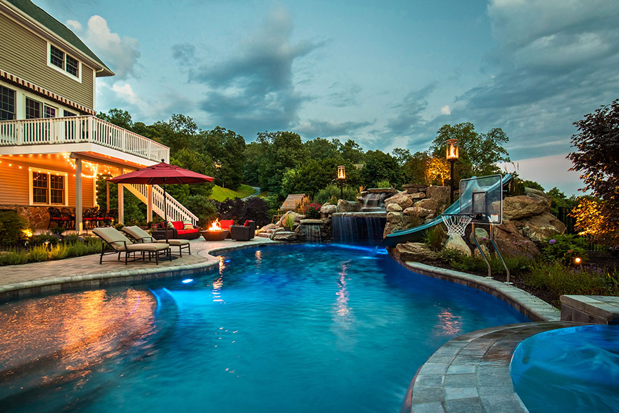 Majestic outdoor pool equipped with a firepit, slide, waterfalls, and pool basketball, exemplifying premier swimming pool remodeling NY, NJ and CT. Close-up view of meticulously placed pool tiles reflecting the high-quality work of New York, New Jersey, and Connecticut swimming pool refinishing services.