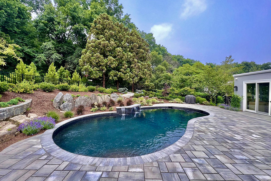 Simple serene pool with a waterfall water feature and natural scenery in the background, showcasing the quality of tri-state pool cleaning services. Simple serene pool with a waterfall water feature and natural scenery in the background, showcasing the quality of tri-state pool cleaning services.