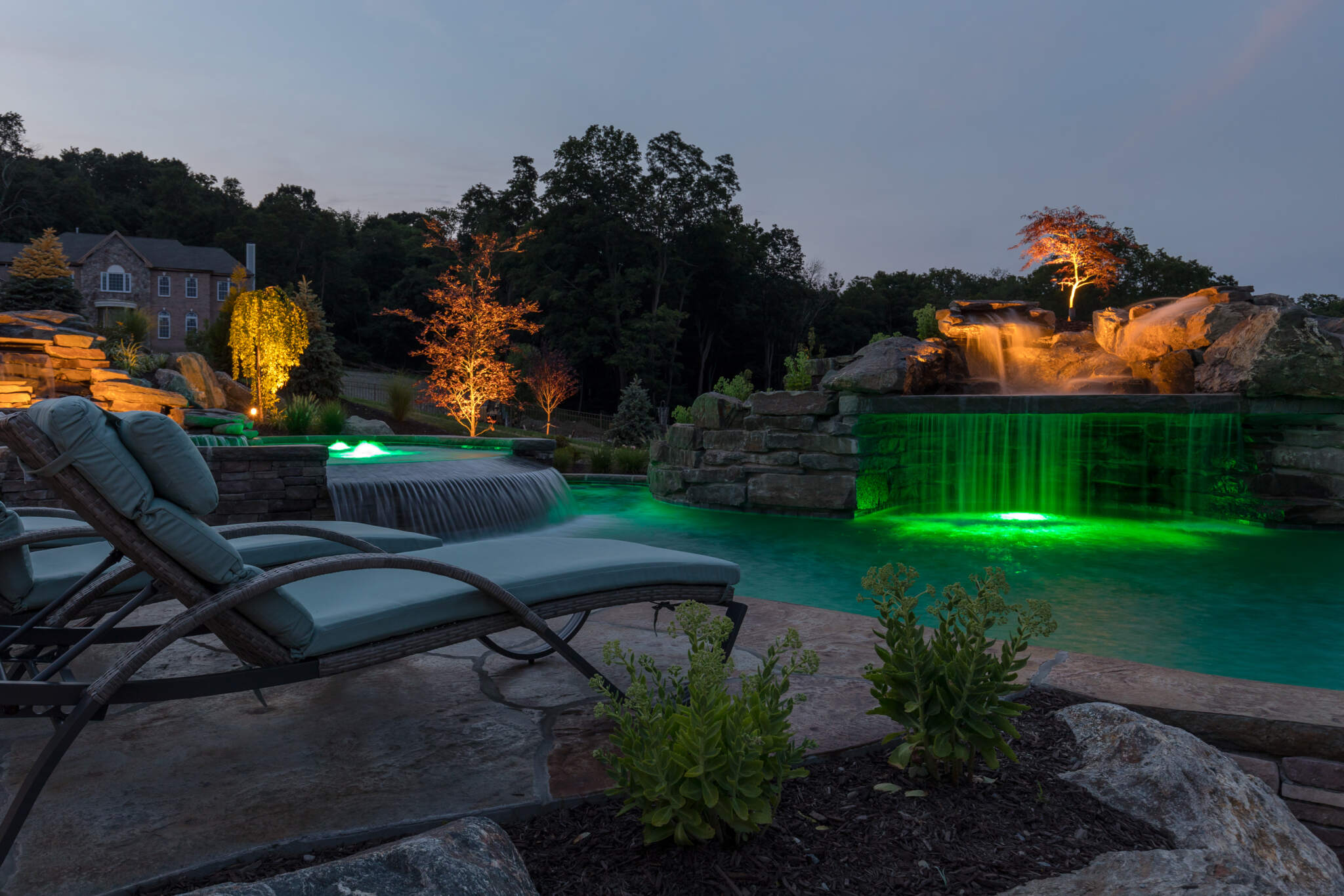 5826d7c0-1e27-48d3-b697-61b3df624708 Natural stone encasing a hot tub and a sublime electrical instalaltion showing limelight with this inground pool design