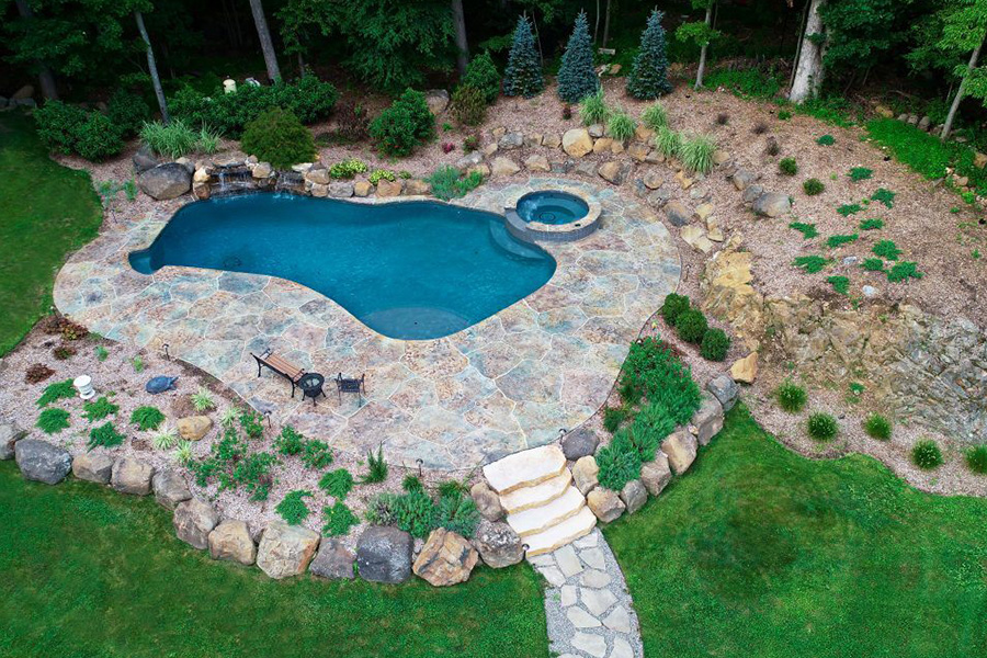 Aerial view of a freeform inground pool spa combo, surrounded by stamped concrete, natural stone, and lush landscaping